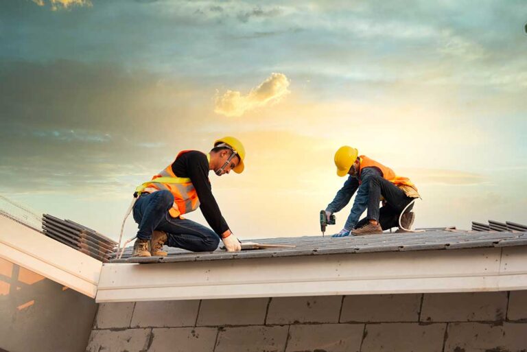 A roof cricket rises behind a chimney, directing rainwater toward metal flashing and roof drainage paths.